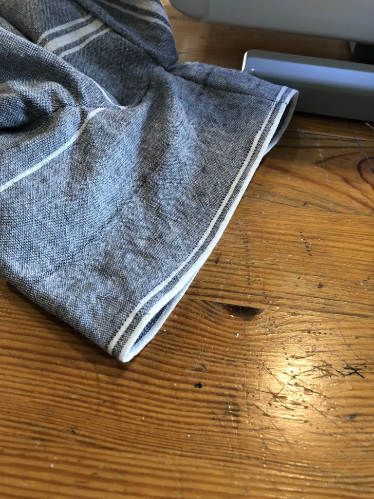 Close up of the sleeve of a gray and white linen striped dress on a wood table